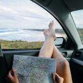 girl with roadmap in car holding her legs out the window